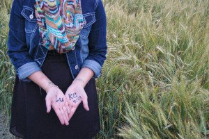 Jena Bea Haney poses in a wheat field with a favorite verse, Luke 9:23, on her hands for her prayer cards. (Jena Bea Haney)