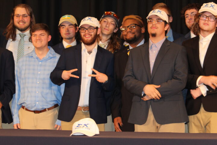 Members of a fraternity pose in behind a hat