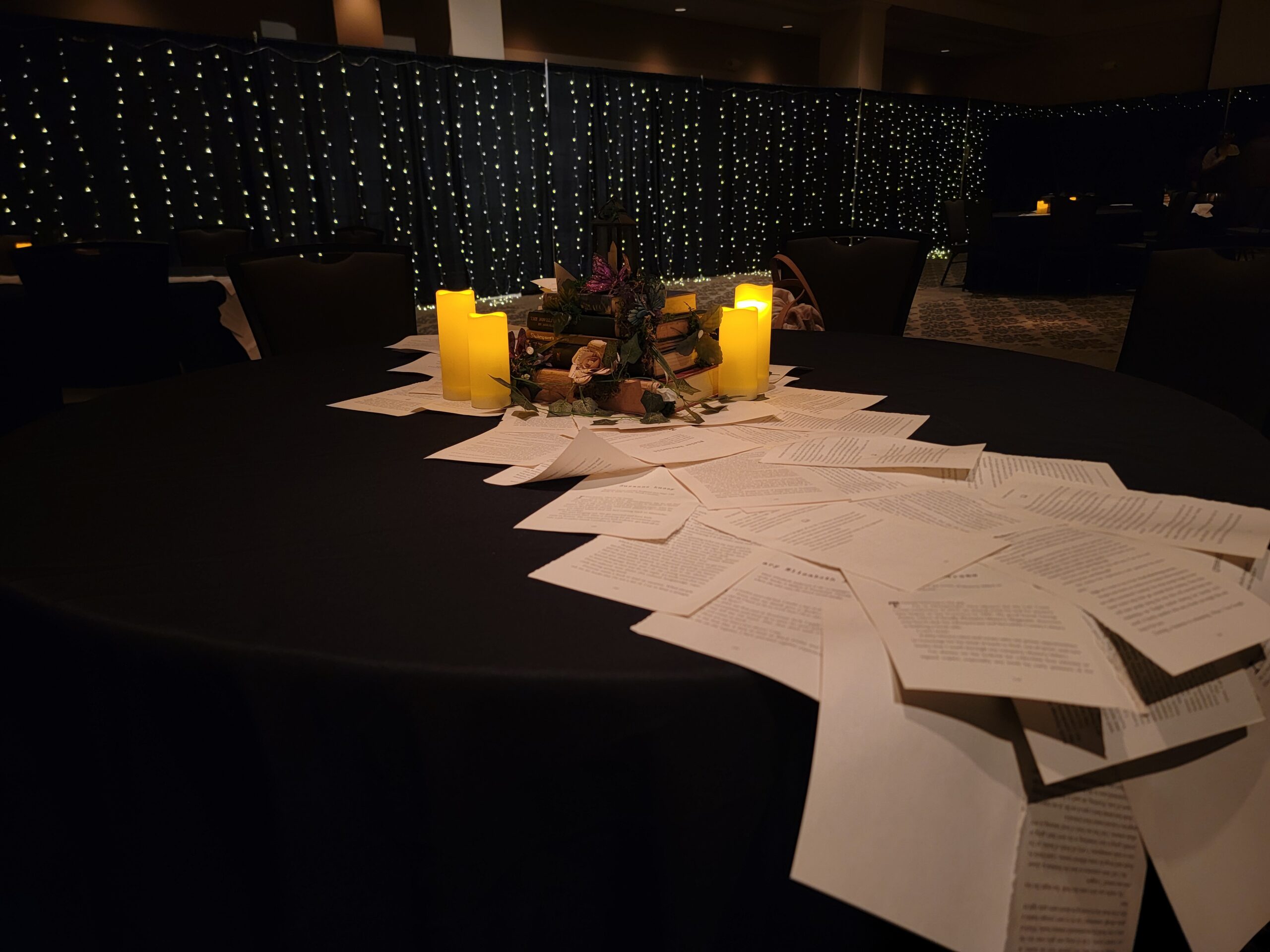 There is a centerpiece made from books and candles with a book page layered train on the table